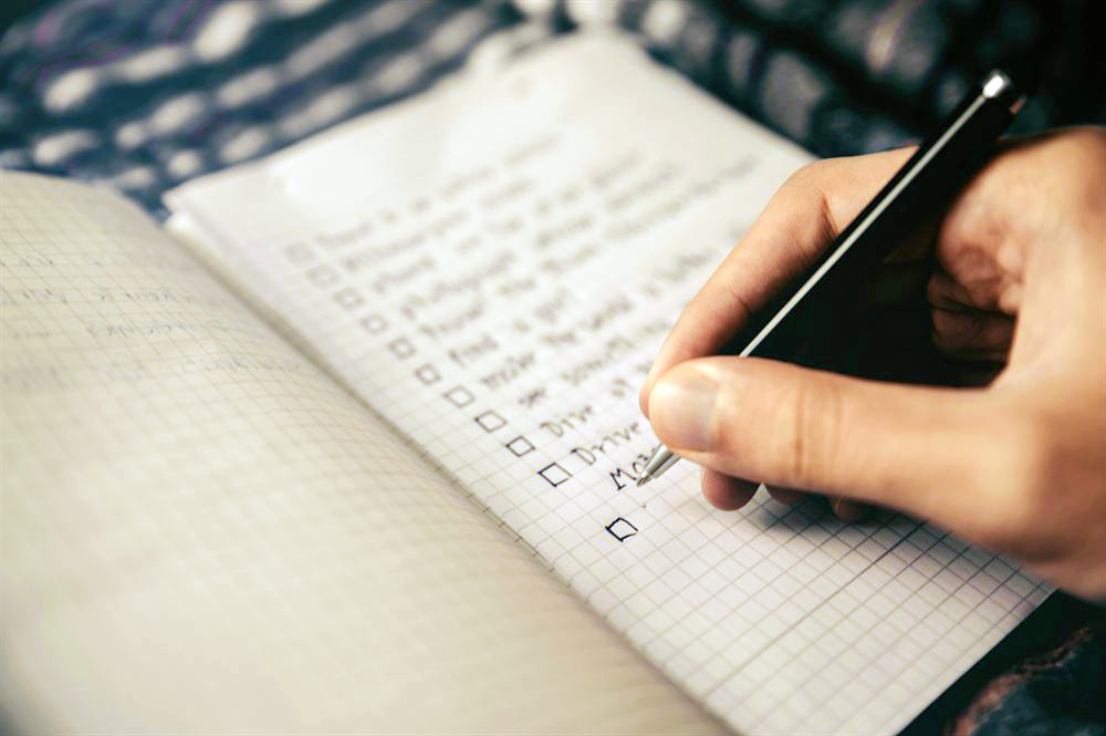 A hand writing a checklist in a squared notebook.